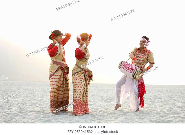 Bihu women dancing as Bihu man plays on a dhol