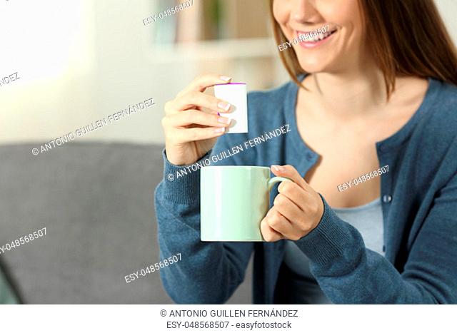 Close up of a woman hands throwing sacharine pill into a mug sitting on a couch in the living room at home