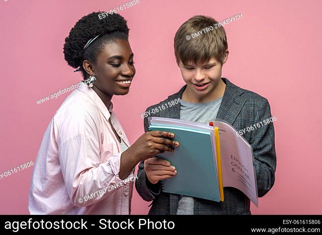 Success. Happy caucasian guy with down syndrome and african american woman holding together looking at notebook standing on light background