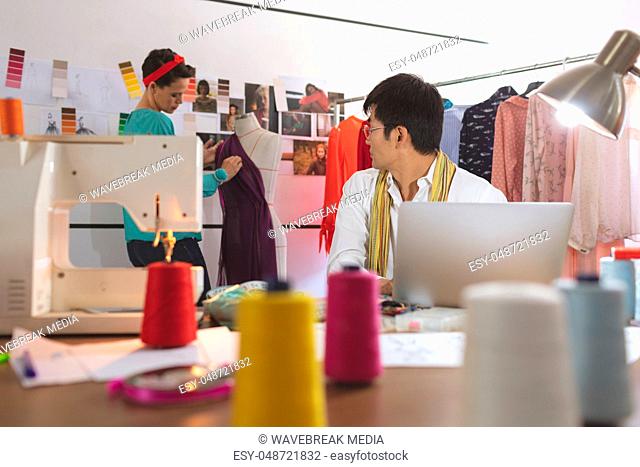Male fashion designer talking with female designer while working on laptop