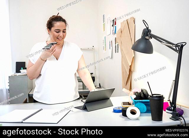 Seamstress working in tailor shop using smartphone and laptop