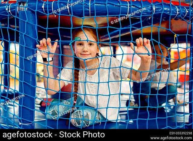 Girl behind the grid in the game maze in the entertainment center. Female child leisures on holidays, childhood happiness, happy kid on playground