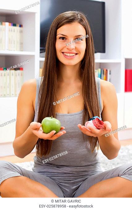 Portrait of young woman holding in hands green apple and tape measure at home. Weight and dieting concept