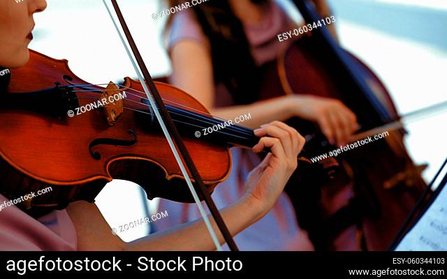 Musical Orchestra Of Female Musicians Plays On The Summer Terrace Outside, Hands Holding A Violin And Bow, Close Up