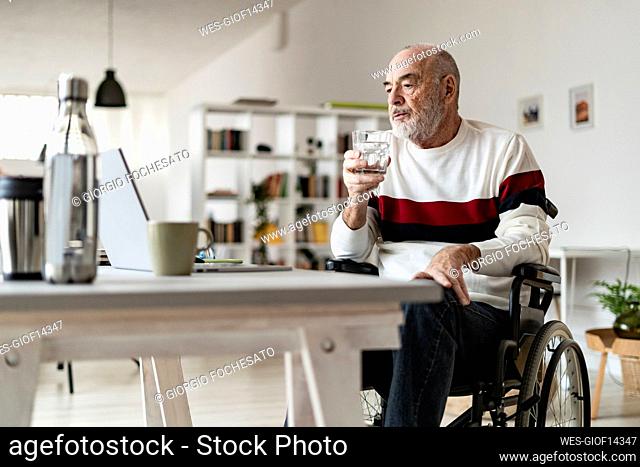 Senior businessman with drinking glass looking at laptop on table