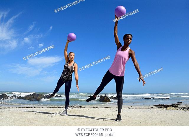 Two women doing fitness exercises with ball on the beach