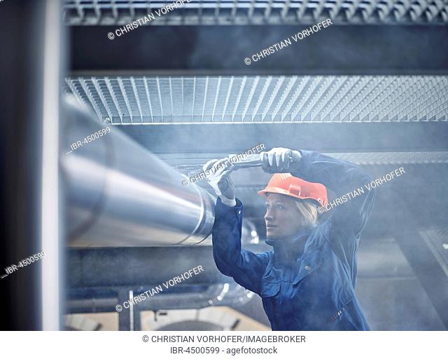 Technician, mechanic with orange helmet mounting a refrigeration line bracket, Austria