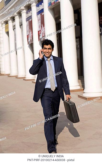 Businessman talking on a mobile phone while walking, Gurgaon, Haryana, India