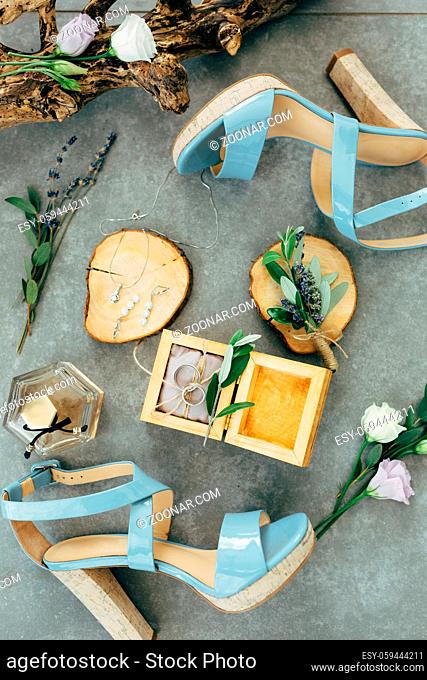 Wedding rings lie in a wooden box surrounded by sandals with heels, flowers and twigs on the floor. High quality photo
