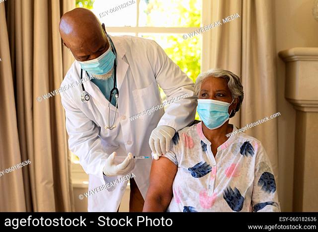 Senior african american woman and male doctor in face masks, woman receiving vaccination