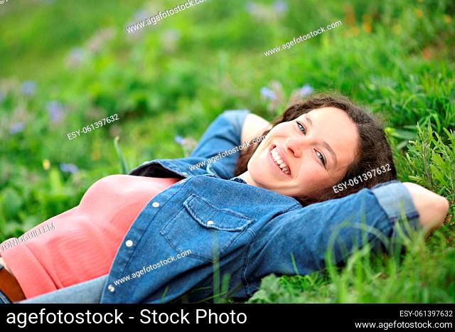 Happy woman relaxing lying on the grass looking at camera in a park