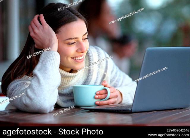 Happy woman watching media content on laptop seated in a coffee shop in winter