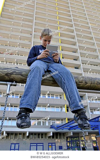 boy playing with gameboy in front of tower block, Germany, Chorweiler , Cologne