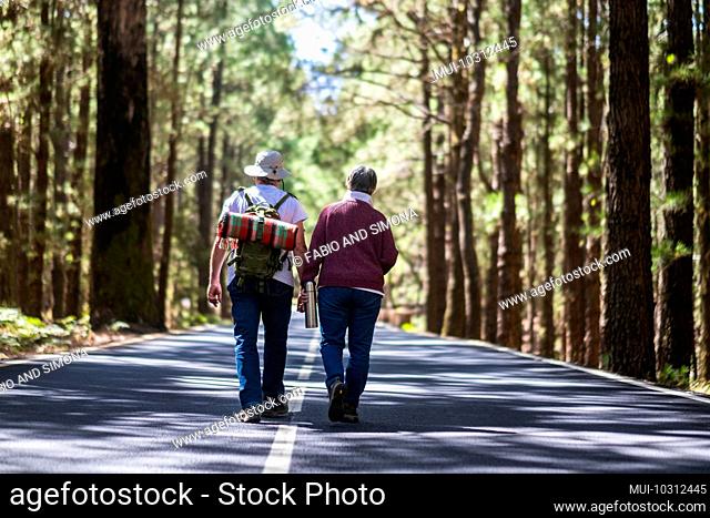 Travel lifestyle for old senior couple walking together in the middle of the road with high trees forest on both sides - lifestyle and togetherness forever life...