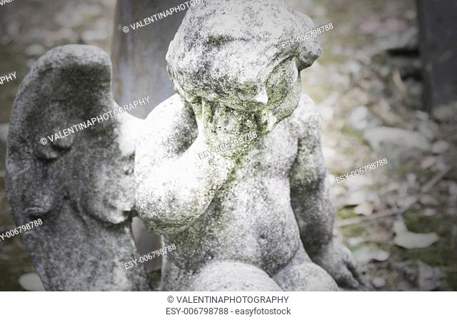 Detail of a beautiful sad small angel statue in a cemetery