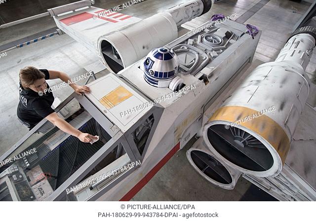 29 June 2018, Germany, Stuttgart: A member of a fan project cleaning the reconstruction of an ""X-Wing"" spaceship from the film saga Star Wars during the...