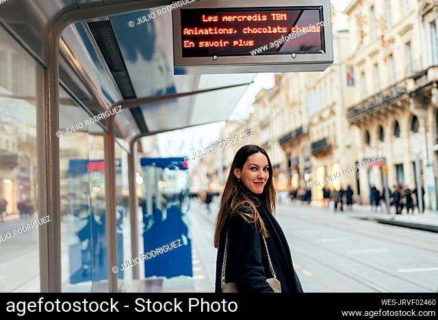 Smiling young woman waiting at tram station in city