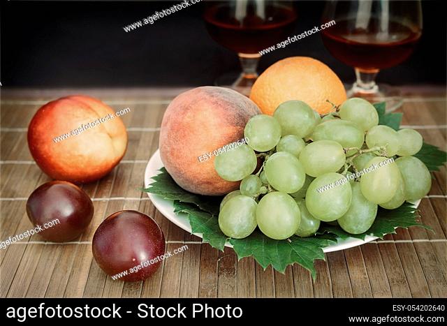 Still life: on the table on a plate are fruits, next to two glasses of wine