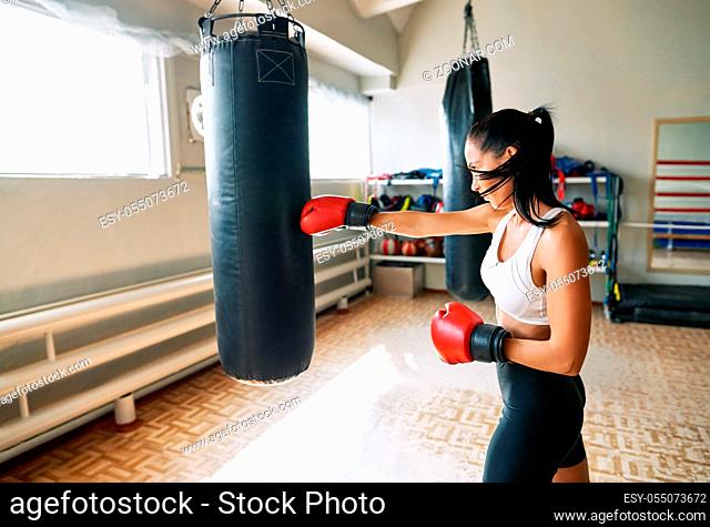 Female boxer hitting a huge punching bag at fitness gym. Woman practicing her punches at a boxing studio