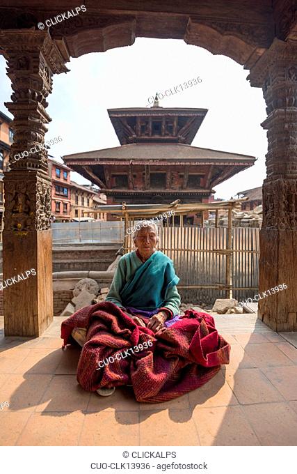 Old lady sitting in prayer under a temple, Bhaktapur, Kathmandu, Bagmati area, Nepal, Asia