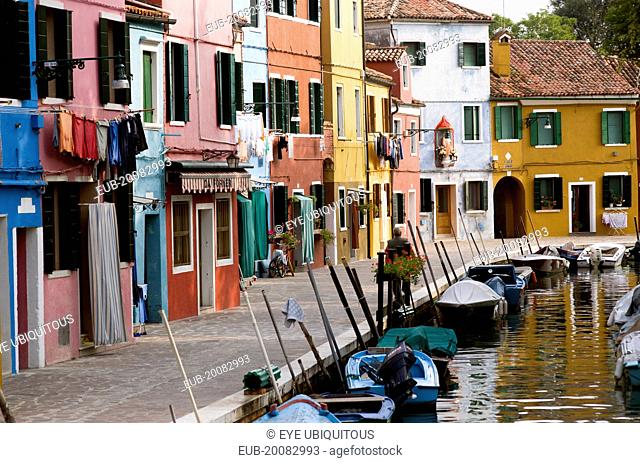 Colourful houses beside a canal on the lagoon island of Burano with boats moored alongside the edge of the canal