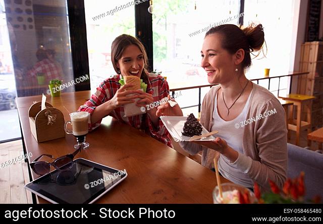 Toned image of happy ladies spending their free time in cafe or restaurant. Pretty women eating sandwich and cafe, drinking coffee