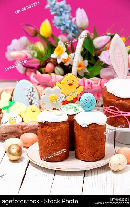 Close-up small traditional Easter breads, glazed and decorated for children with ginger breads in chicken shape. Basket with bright colorful flowers on...
