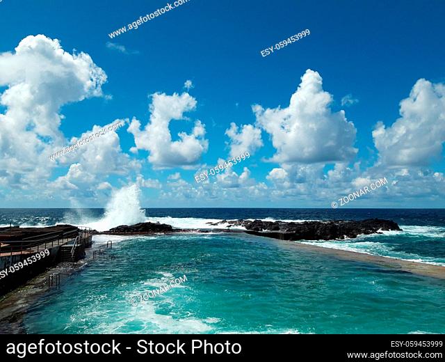 ocean wave splash on rocks at coast on a sunny day with blue sky