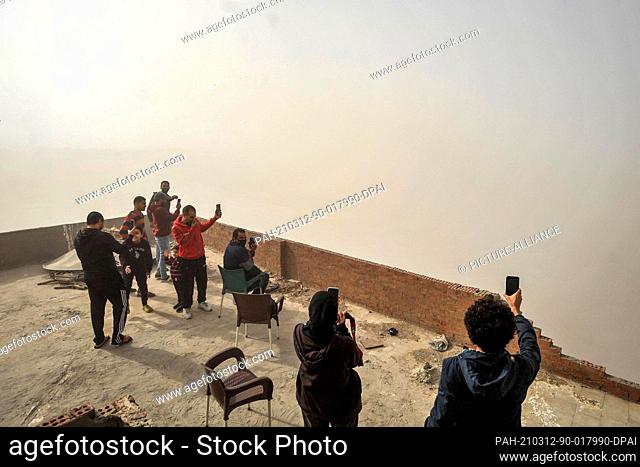 12 March 2021, Egypt, Kafr Tohormos: People take pictures of a 14-story building as it collapses during a controlled explosion operation carried out by Egyptian...