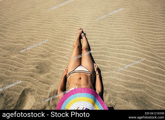 Nice body female laying on the sand at the beach with colorful straw hat enjoying summer holiday vacation alone in bikini - people outdoor relax time taking...