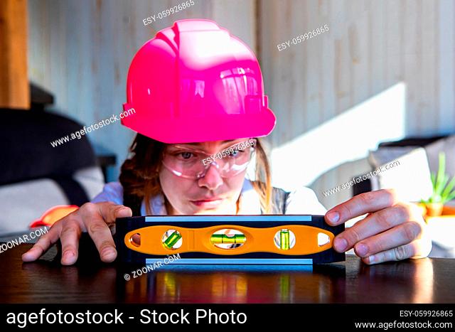 young caucasian woman architect wearing a pink hard hat and protective eyewear, she measuring horizontal surface with a spirit bubble level tool