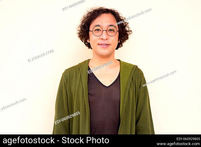 Portrait of Japanese man with curly hair wearing eyeglasses against concrete wall