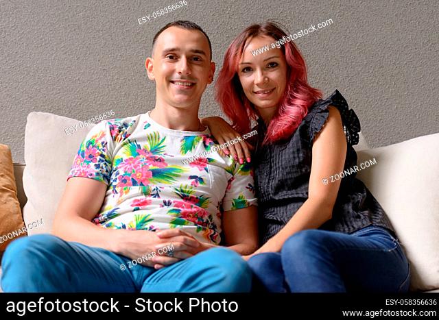 Portrait of handsome man and beautiful woman with pink hair as couple together in the living room at home
