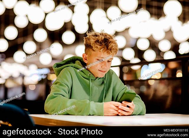 Smiling boy using smart phone in illuminated food court