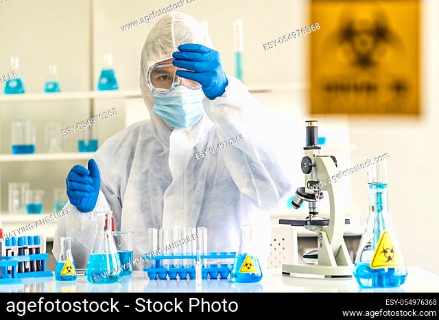 Scientists hold test tube and examine for his research and develop vaccine for coronavirus covid-19 pandemic in Laboratory room with caution signage