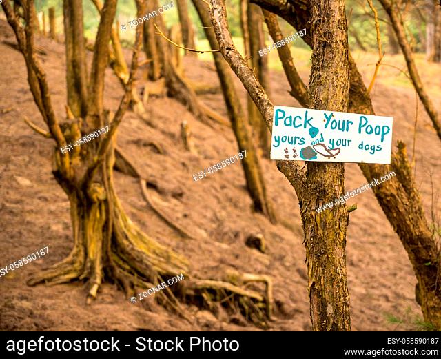 Pick up or pack your poop sign on tree advising people to not leave waste on the ground in forest
