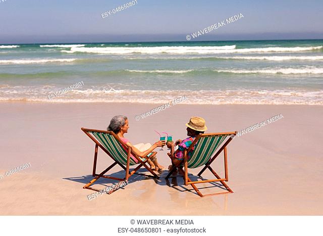 Senior couple relaxing on sun lounger and toasting cocktail glasses on beach