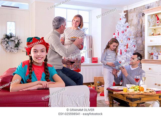 Three Generation Family at Christmas Time. Young Girl is looking at the Camera and Smiling while the family chat in the background