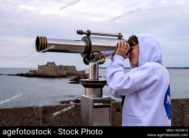 france, brittany, ille et vilaine, saint malo, boy looks through a telescope, tidal island petit-bé with the fort national, atlantic coast