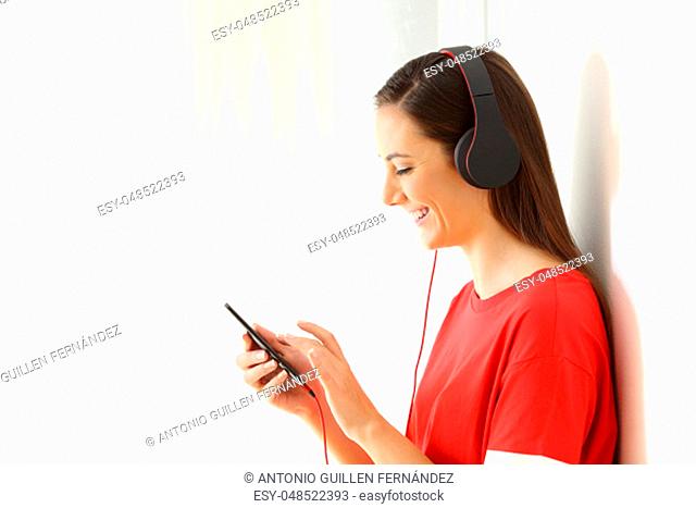 Side view portrait of a girl listening to music on line with a smart phone and headphones isolated on white at side
