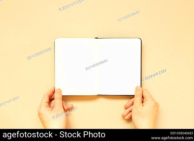 Hands open note book on beige background. top view, copy space