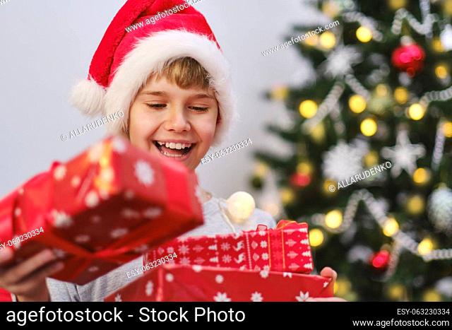 Portrait of an excited boy holding presents by the Christmas tree on Christmas morning. Christmas happiness