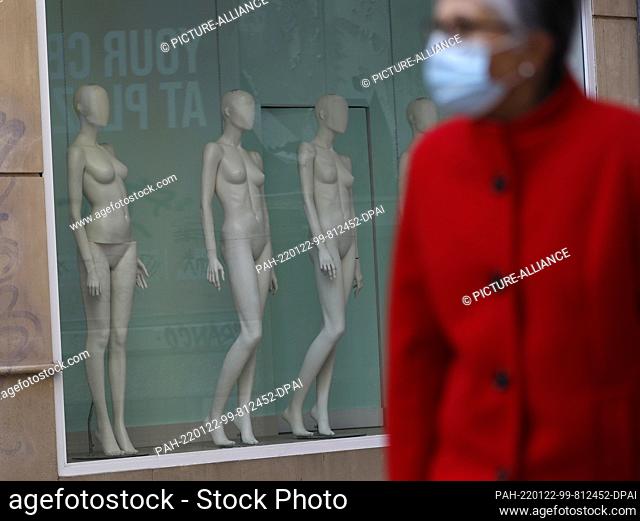 22 January 2022, Spain, Palma: A woman wearing a protective mask walks past a closed store in Palma. The 14-day incidence in Mallorca is currently 3239 people...