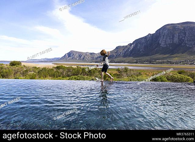 Eight year old boy walking around the edge of an infinity pool, a mountain backdrop