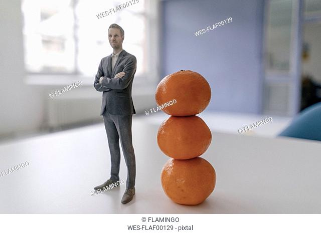 Miniature businessman figurine standing next to clementines