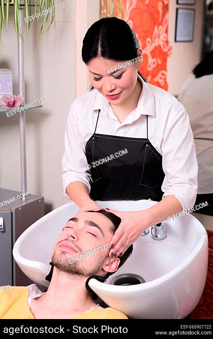 Picture of hairdresser washing handsome man#39;s hair in beauty saloon. Handsome man in hairdressing saloon
