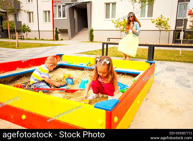 Little children playing at modern sandbox with toys. Young happy family on a walk