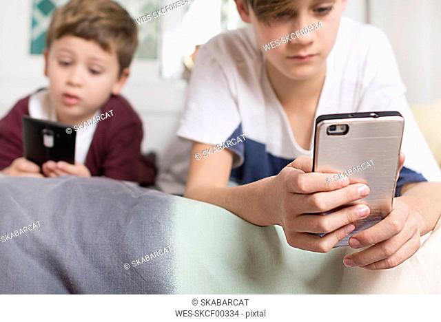 Two boys lying on bed at home using cell phones