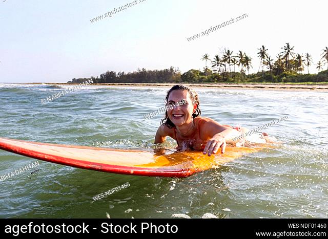 Happy woman lying on surfboard in sea at beach