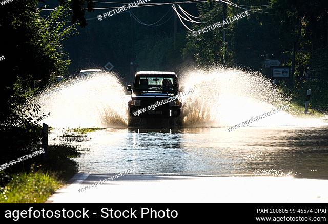 05 August 2020, Bavaria, Raubling: A car drives over a road that is under water due to the heavy rainfall of the past days. Photo: Peter Kneffel/dpa
